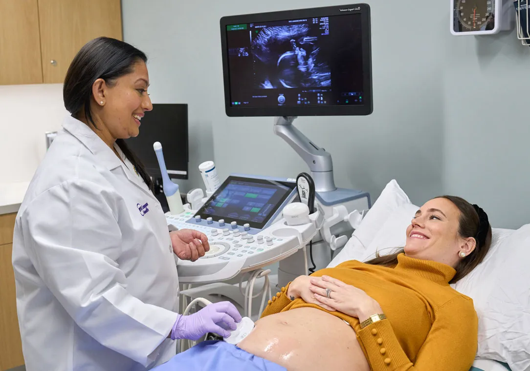 A pregnant woman lying on an exam table looks at Dr. Geeta Sharma as she performs an ultrasound.
