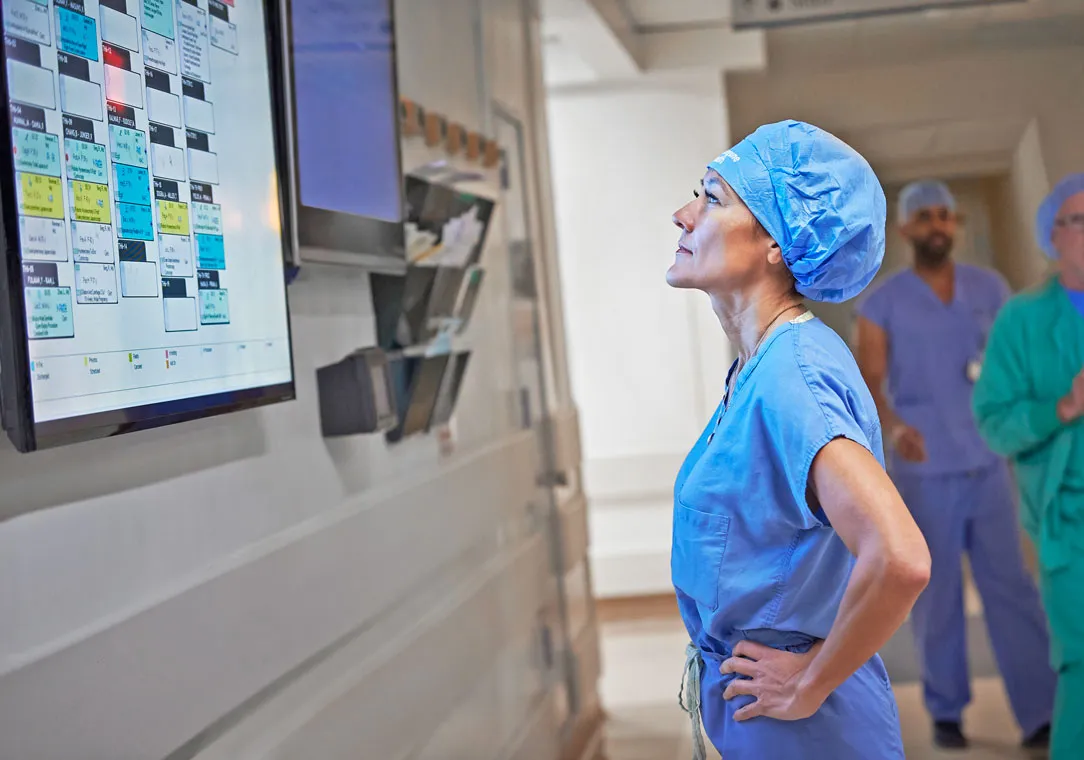 Dr. Christine Ren-Fielding, in surgical scrubs, looks at a screen hanging on the wall in a medical facility.
