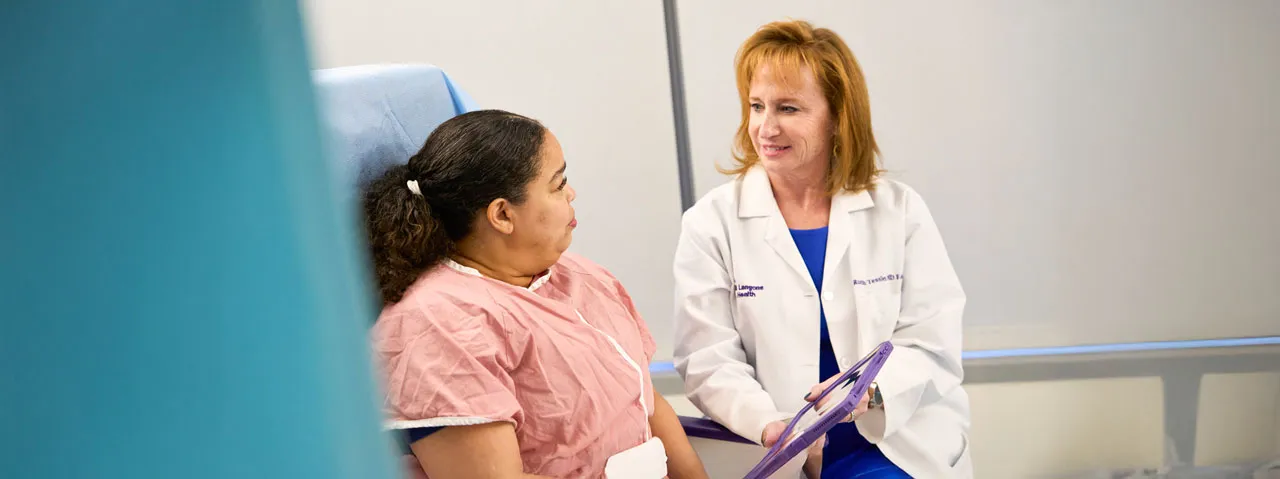 Dr. Ruth Tessler holds an electronic tablet and speaks with a patient sitting in an exam room. 