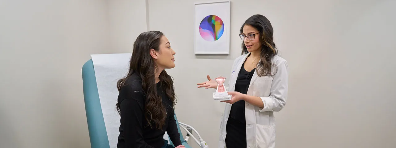 Dr. Sarah Shawki holds a model of the female reproductive system as she talks with a patient sitting in an exam room. 
