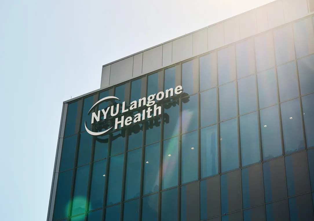 The corner of an NYU Langone Health building against a bright blue sky.