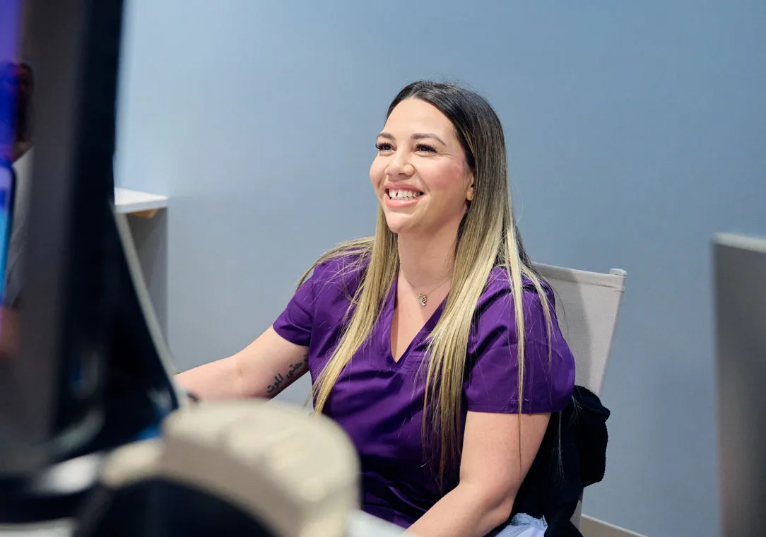 A woman sits at a reception desk in front of a computer monitor.