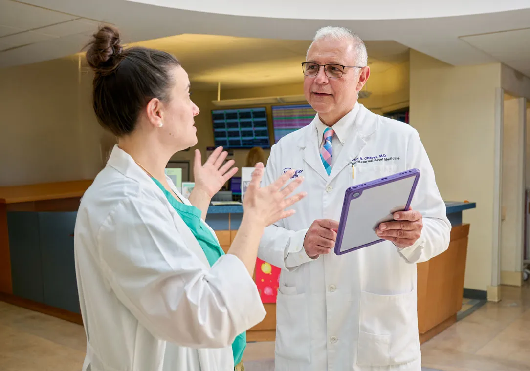 Dr. Nina Amelio-Simulcik gestures toward and Dr. Martin Chavez, who is holding a clipboard, as they talk.